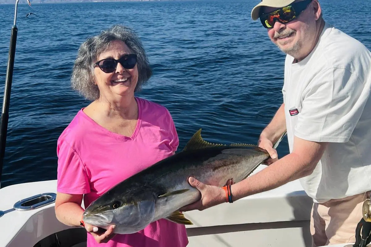 Two people holding a large fish on a boat by the ocean.