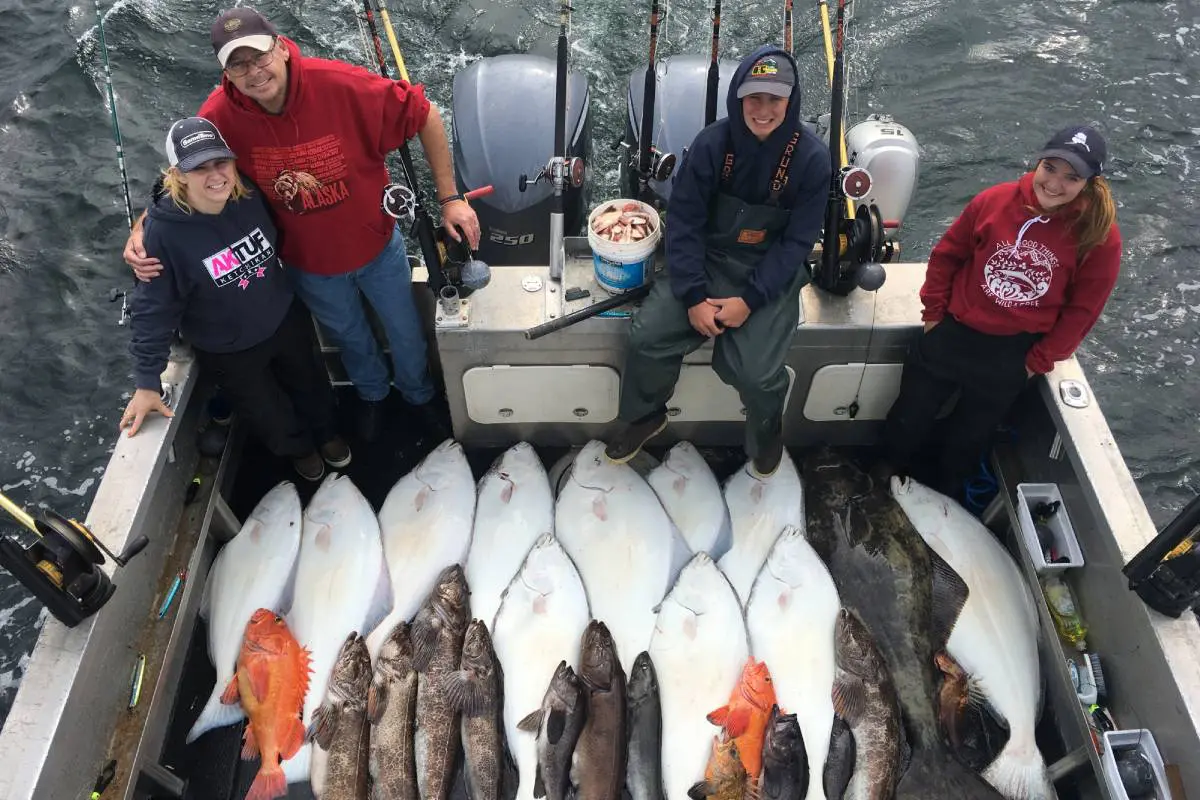 Group posing with a diverse catch of fish by the water.